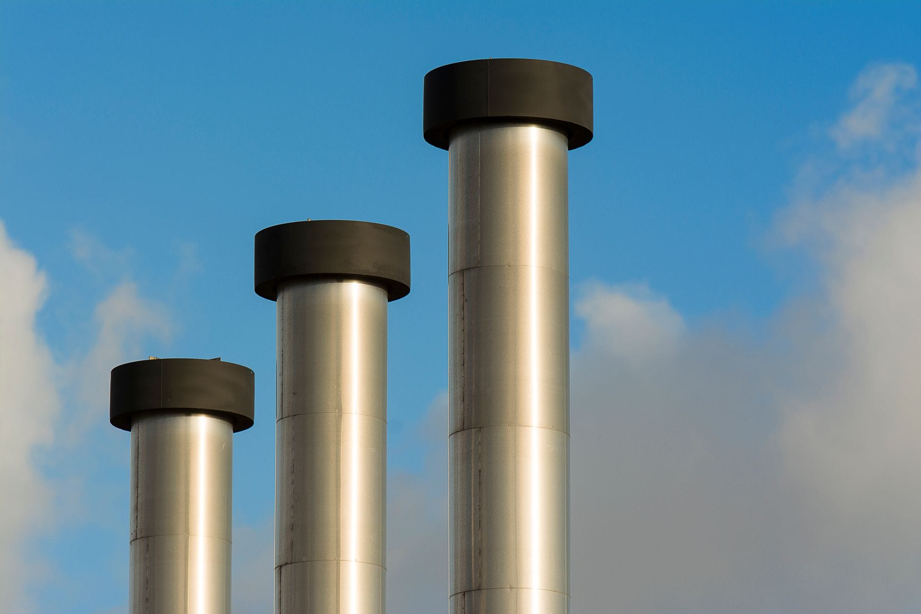 Three metallic chimneys reaching into a clear blue sky, exemplifying industrial architecture.